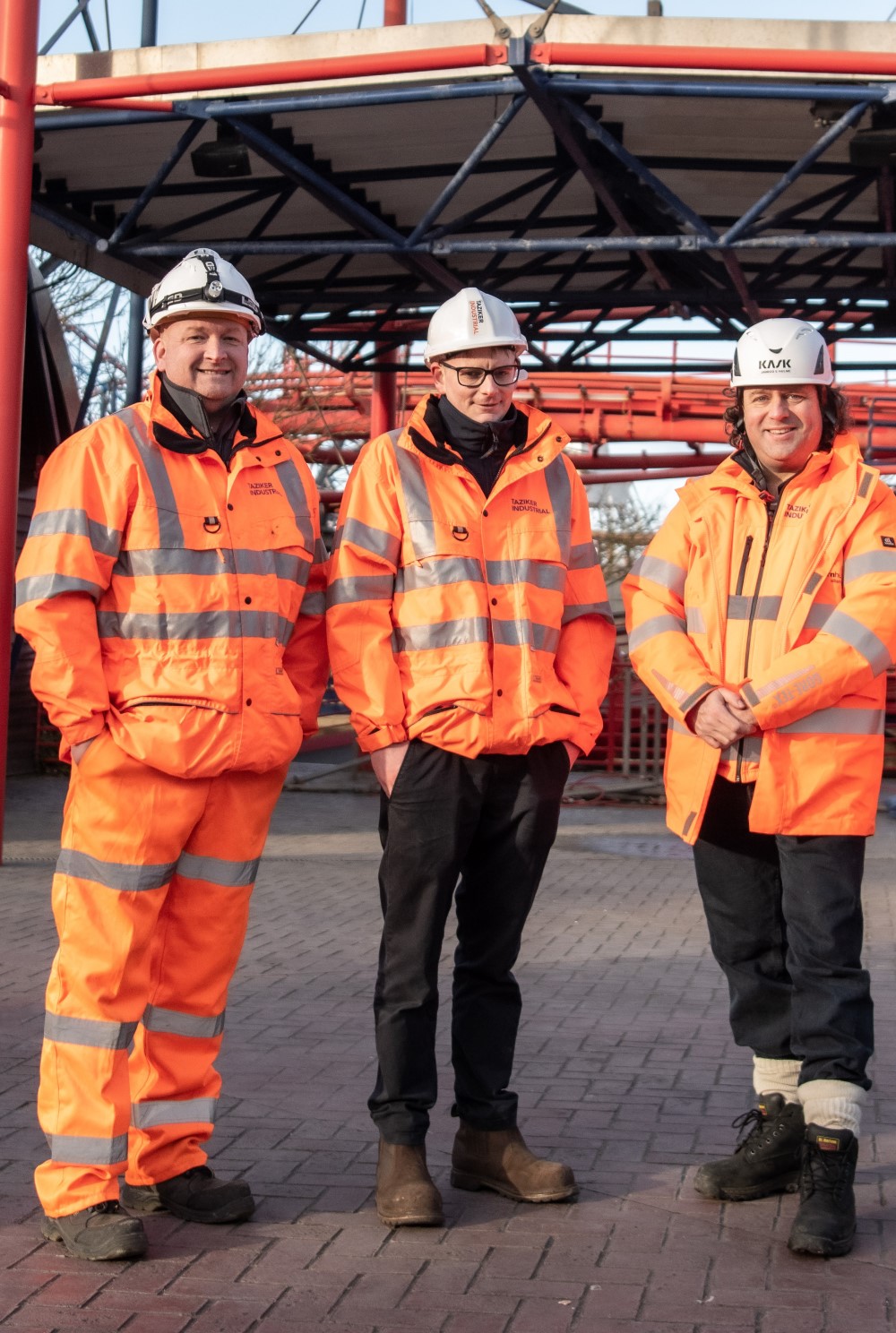 Three Taziker workers in PPE next to the Big One rollercoaster.