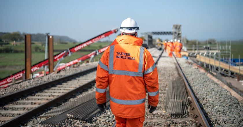 Construction worker in Taziker branded PPE walking on train track.