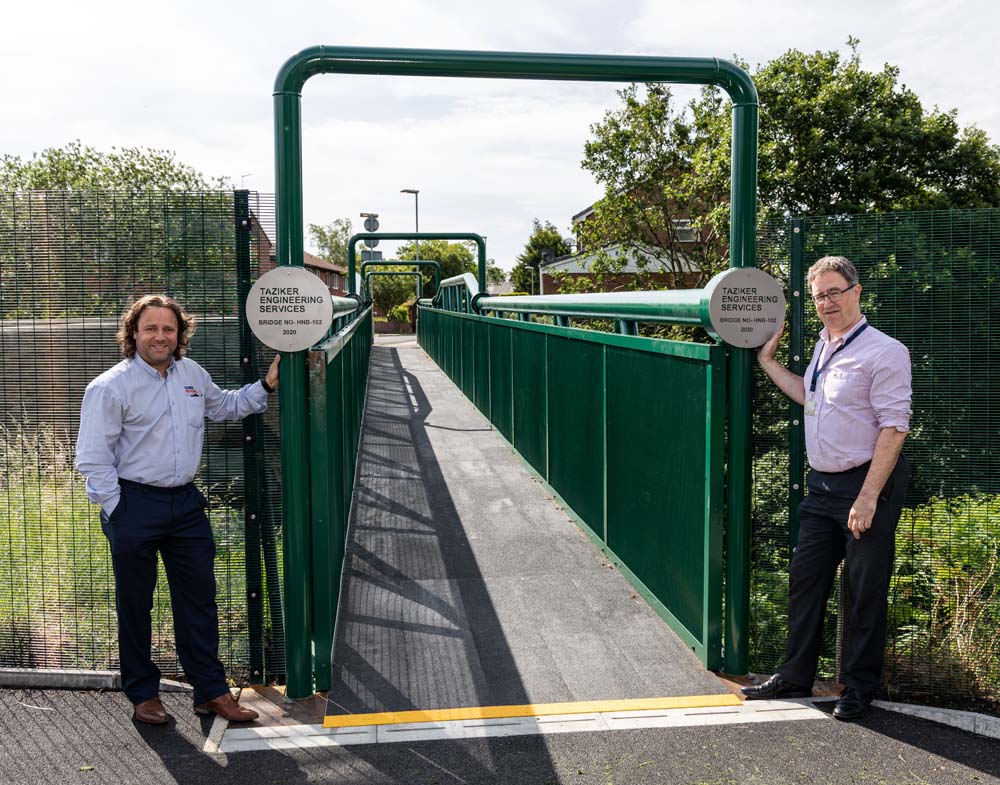 Two men standing next to new green footbridge.