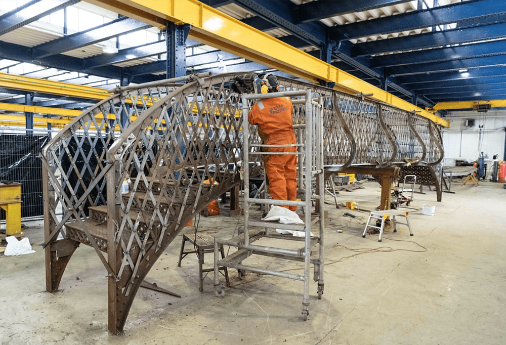 Taziker construction worker in orange PPE working on new Heywood footbridge in their fabrication facility.