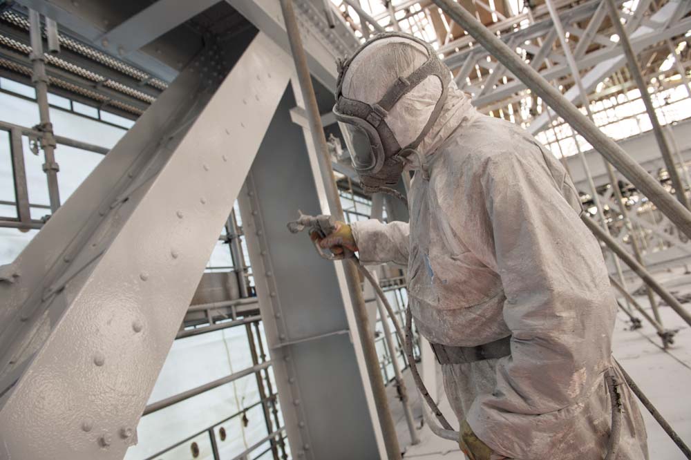 Man wearing white PPE painting the Royal Albert Bridge inside encapsulation.