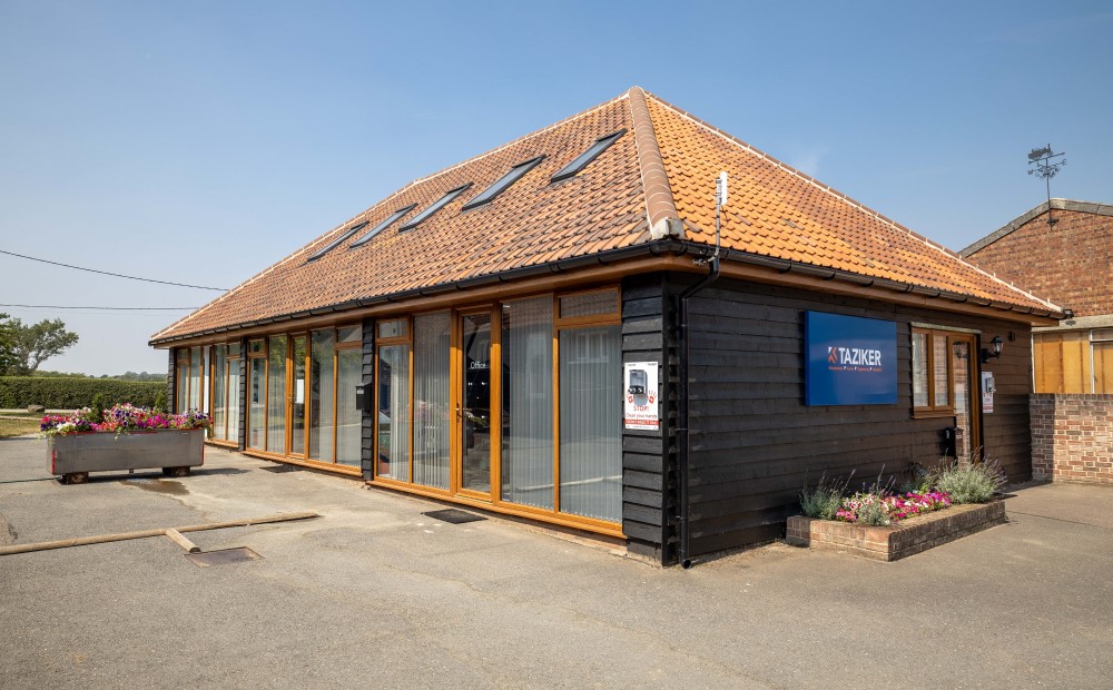 Black wooden panel office with brown roof, large windows and Taziker sign.