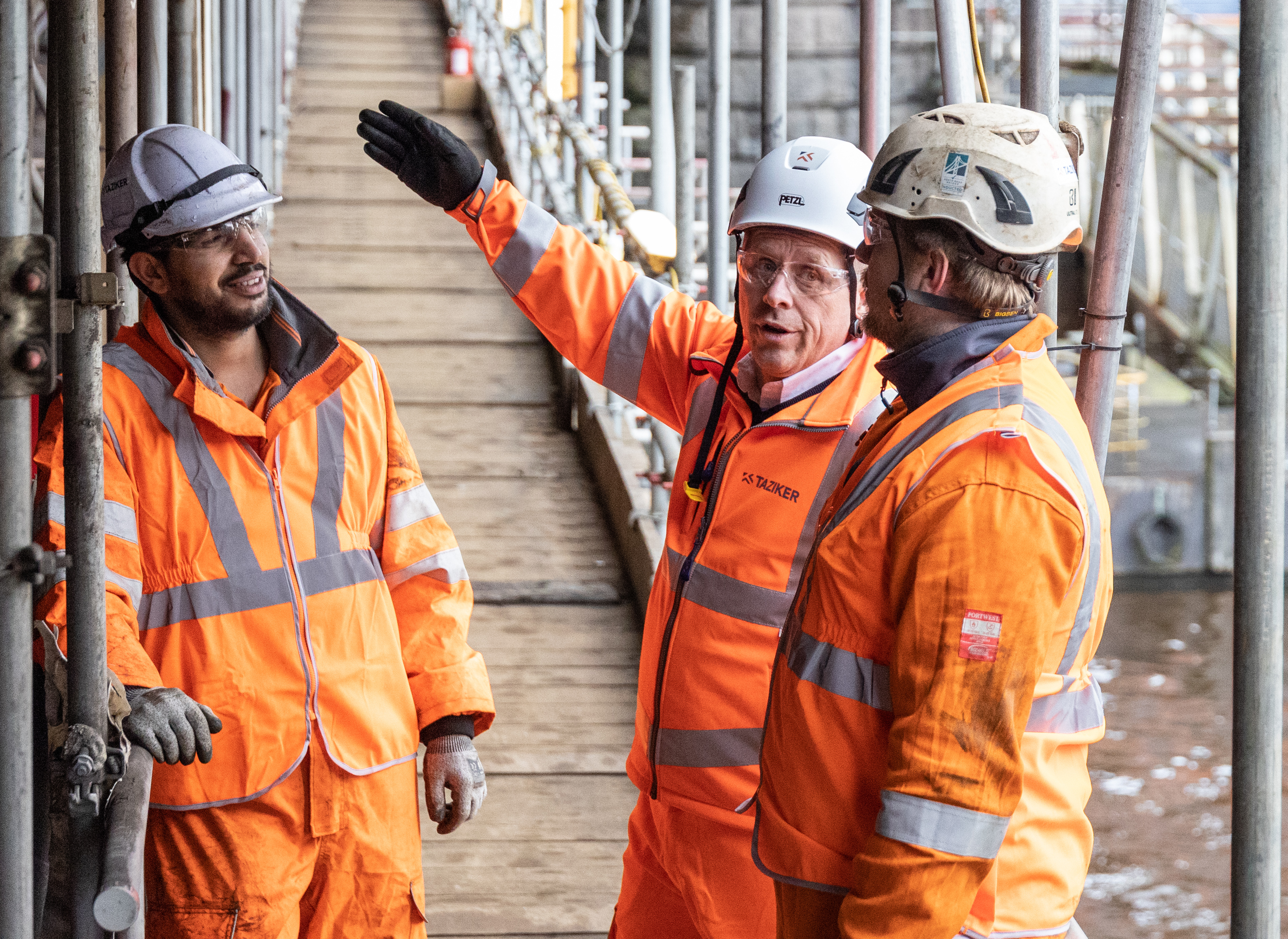 Three men in PPE on a bridge with scaffolding.