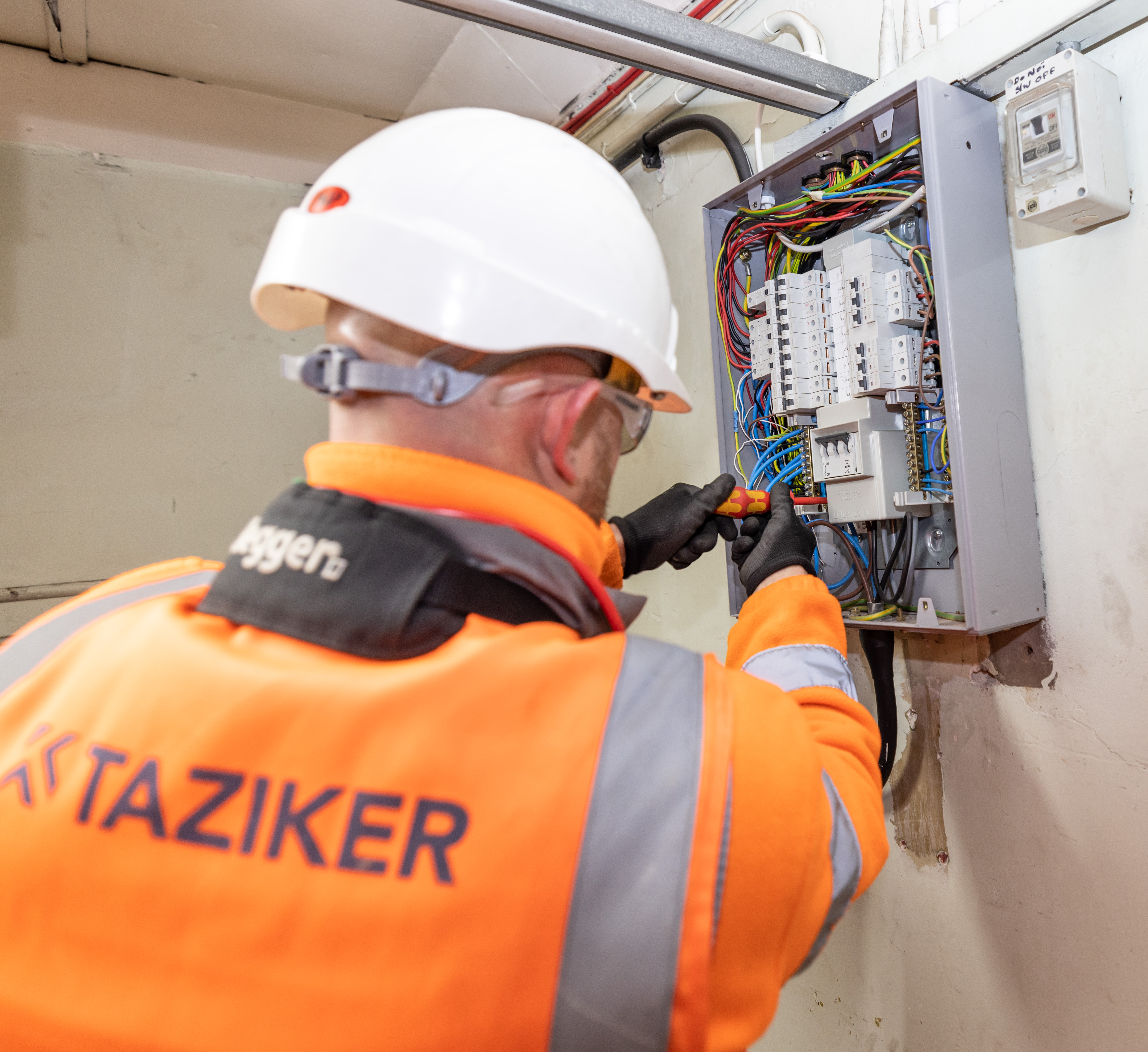Electrician wearing Taziker branded PPE carrying out electrical works on a fuse box.