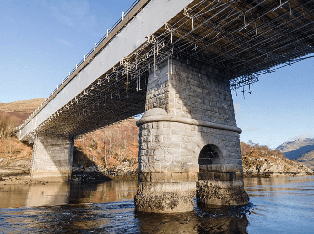 Encapsulation of large stone bridge over water with blue skies.